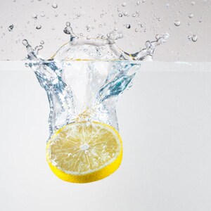May include: A yellow lemon wedge splashing into clear water, creating a crown of water droplets.