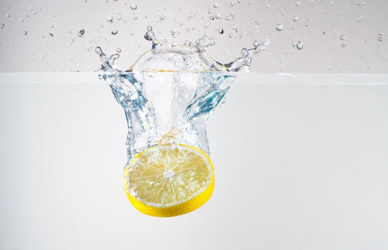 May include: A yellow lemon wedge splashing into clear water, creating a crown of water droplets.