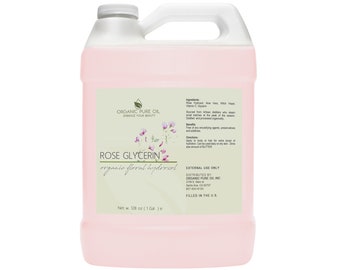 Puede incluir: Una jarra de un galón de hidrolato floral orgánico de rosa y glicerina. La etiqueta es blanca con texto verde y un diseño floral rosa. La jarra está llena de un líquido rosa claro. La etiqueta incluye los ingredientes: hidrolato de rosa, aloe vera, hamamelis y glicerina. La etiqueta también incluye instrucciones de uso e información sobre el distribuidor, Organic Pure Oil Inc.