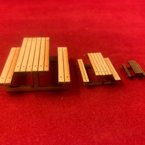 May include: Three wooden picnic tables of different sizes. The largest table has two benches attached to the sides. The smallest table is a miniature version of the larger table.