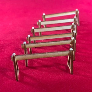 Puede incluir: Un conjunto de seis barreras de madera de estilo caballete, dispuestas en fila sobre una superficie roja. Las barreras son de madera marrón claro y miden aproximadamente 25 cm de largo.