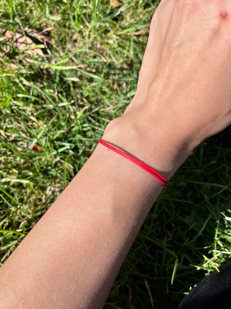 May include: A red string bracelet worn on a person's wrist.