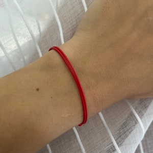 May include: A red string bracelet worn on a person's wrist.
