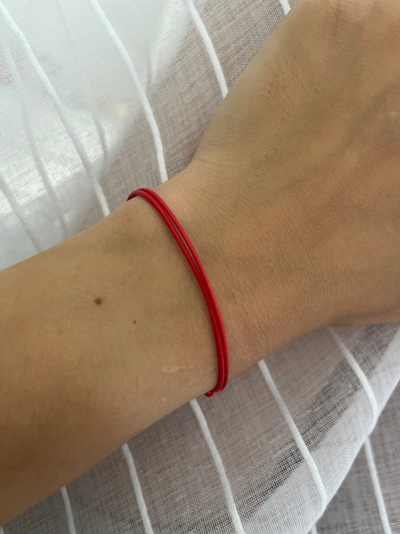 May include: A red string bracelet worn on a person's wrist.