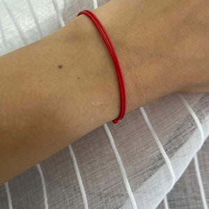 May include: A red string bracelet worn on a person's wrist.
