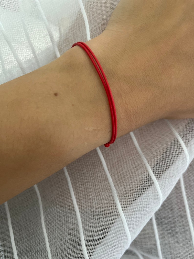 May include: A red string bracelet worn on a person's wrist.