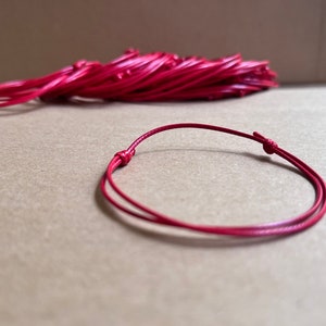 May include: A red cord bracelet with a simple knot closure. The bracelet is made of a thin, flexible cord and is approximately 7 inches in length.