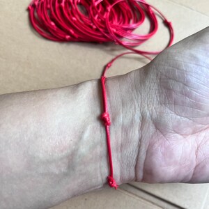 May include: A red string bracelet tied in a knot on a person's wrist.
