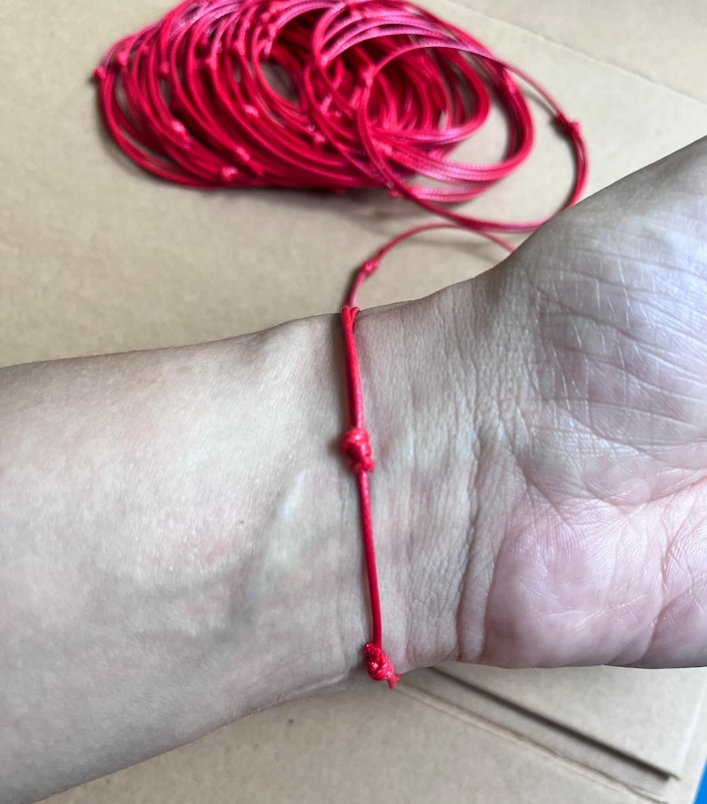 May include: A red string bracelet tied in a knot on a person's wrist.