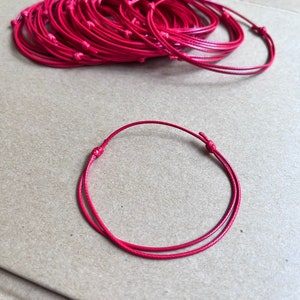 May include: A pile of red string bracelets, with one bracelet laid out on a brown surface.