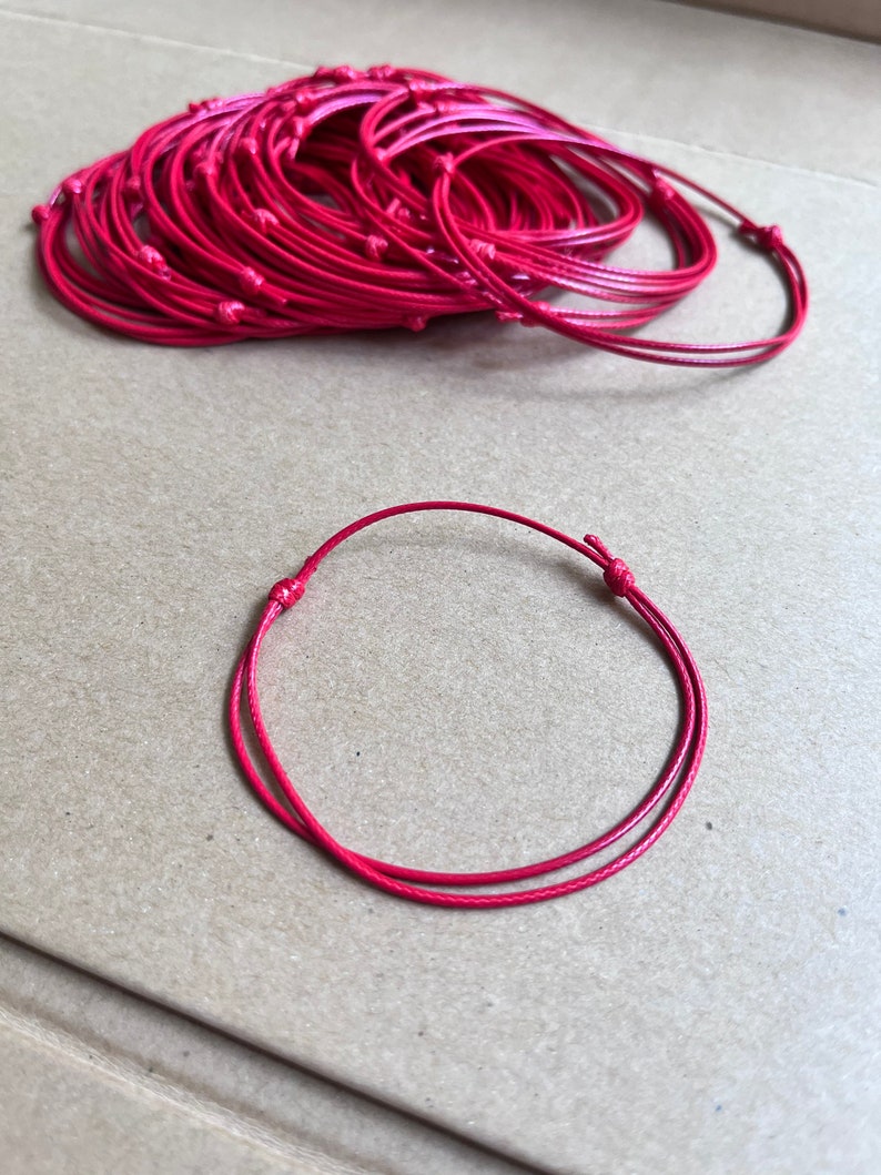 May include: A pile of red string bracelets, with one bracelet laid out on a brown surface.