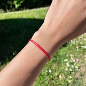 May include: A red string bracelet worn on a person's wrist.