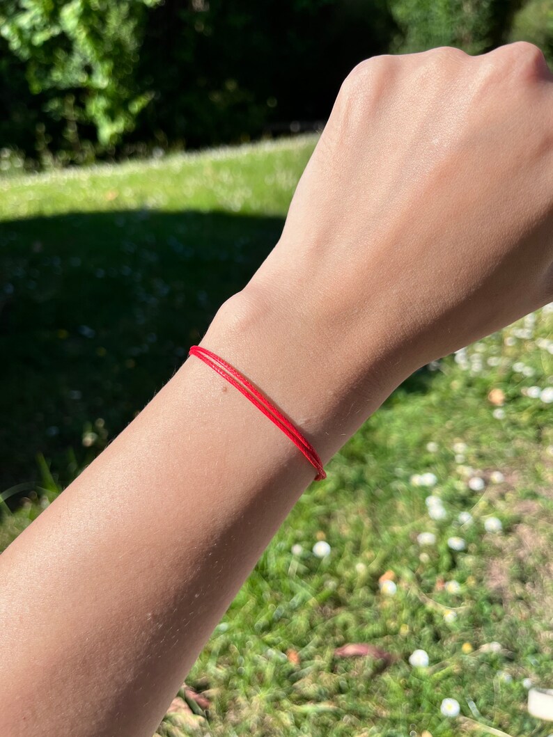May include: A red string bracelet worn on a person's wrist.