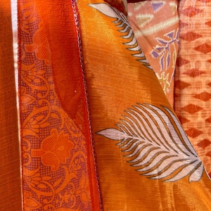 Pode incluir: Close-up de um tecido colorido com uma variedade de padr&otilde;es, incluindo desenhos florais e geom&eacute;tricos. O tecido &eacute; laranja, vermelho, branco e verde.
