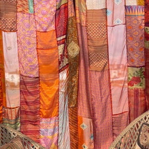 Pode incluir: Uma cortina de patchwork colorida feita de v&aacute;rios tecidos em tons de laranja, vermelho, rosa e roxo. A cortina &eacute; feita de muitos peda&ccedil;os de tecido diferentes costurados juntos, criando um visual &uacute;nico e ecl&eacute;tico.