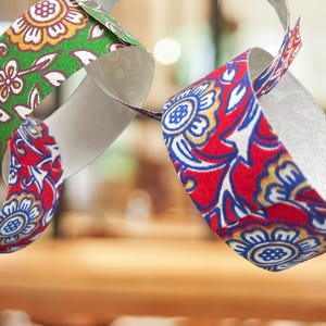 May include: Close-up of a paper chain with colorful floral patterns. The chain links are red, green, and white, with gold and blue accents. The design features stylized flowers and leaves, creating a festive and decorative look.