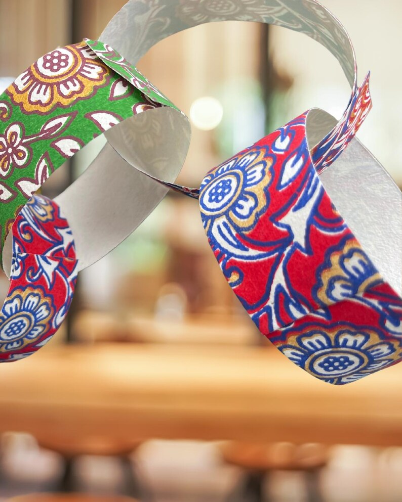 May include: Close-up of a paper chain with colorful floral patterns. The chain links are red, green, and white, with gold and blue accents. The design features stylized flowers and leaves, creating a festive and decorative look.