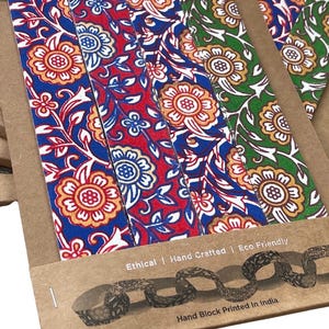 May include: Close-up of several floral patterned bookmarks in blue, red, and green. The bookmarks are made of fabric and are packaged in brown cardboard. The text "Ethical | Hand Crafted | Eco Friendly" and "Hand Block Printed In India" are visible.