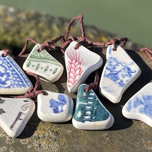 May include: A collection of eight ceramic pendants, each with a unique design. The pendants are white with various blue, green, and red patterns. They are strung on brown cords and would make a unique gift.