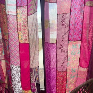 May include: Patchwork curtains in shades of pink and magenta. The curtains are made of various fabrics with different patterns and textures, including floral and geometric designs. The panels are sewn together, creating a unique and colorful window treatment.