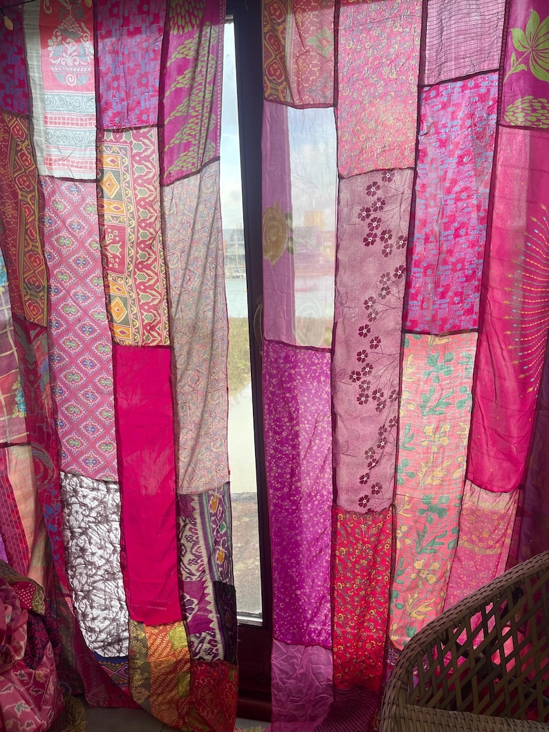 May include: Patchwork curtains in shades of pink and magenta. The curtains are made of various fabrics with different patterns and textures, including floral and geometric designs. The panels are sewn together, creating a unique and colorful window treatment.