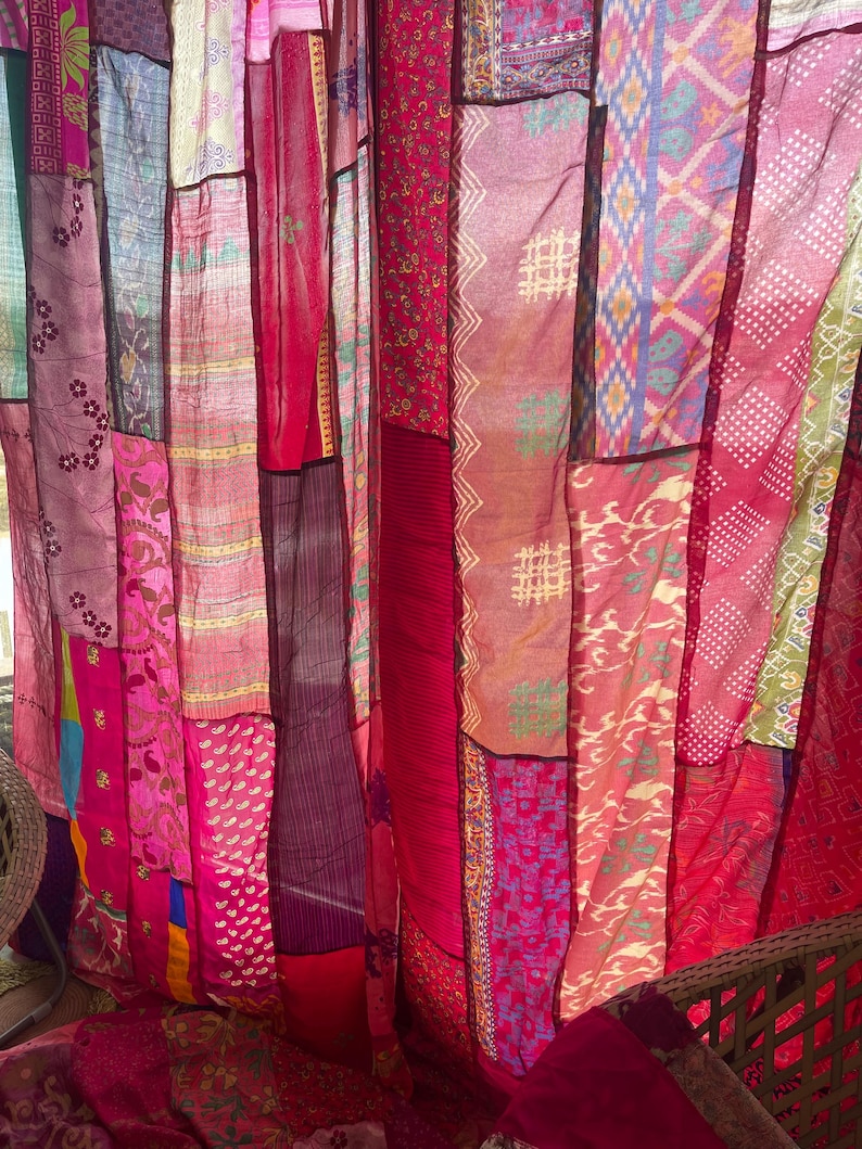 May include: A patchwork curtain made of various fabrics in shades of red, pink, and purple. The fabrics have different patterns, including floral, geometric, and abstract designs. The curtain is hanging, and the light shines through the sheer materials.