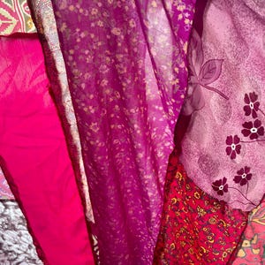 May include: A vibrant display of colorful fabrics in shades of pink, fuchsia, and purple. The textiles feature floral patterns, intricate designs, and varying textures, creating a visually rich and layered composition. The fabrics are likely used for clothing or home decor.