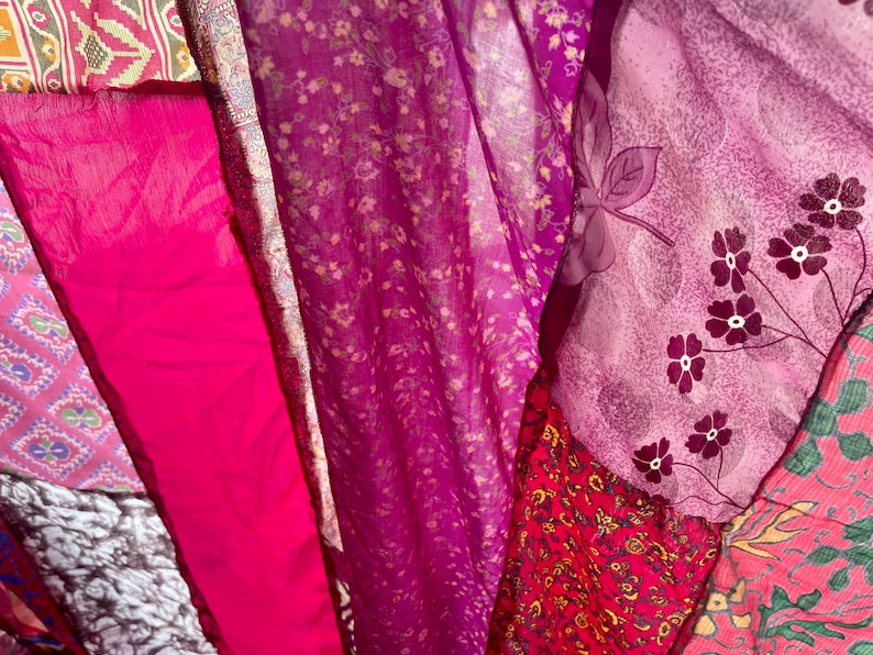 May include: A vibrant display of colorful fabrics in shades of pink, fuchsia, and purple. The textiles feature floral patterns, intricate designs, and varying textures, creating a visually rich and layered composition. The fabrics are likely used for clothing or home decor.
