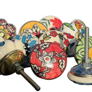 May include: A collection of round ceramic cabinet knobs featuring various hand-painted floral and geometric patterns in vibrant colors including red, blue, green, and yellow. Each knob includes a metal bolt and nut for installation purposes.