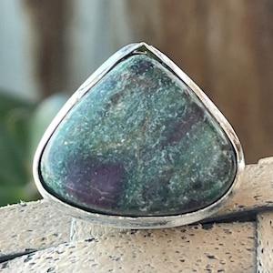 Könnte beinhalten: Ein silberner Ring mit einem dreieckigen grünen Edelstein, der in der Mitte eingesetzt ist. Der Edelstein hat eine marmorierte, gefleckte Optik.