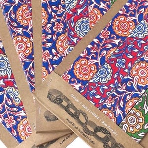 May include: Close-up of several notebooks with colorful floral patterns in red, blue, and orange. The notebooks are in cardboard covers with text that reads "Ethical | Hand Crafted | Eco Friendly" and "Hand Block Printed in India."