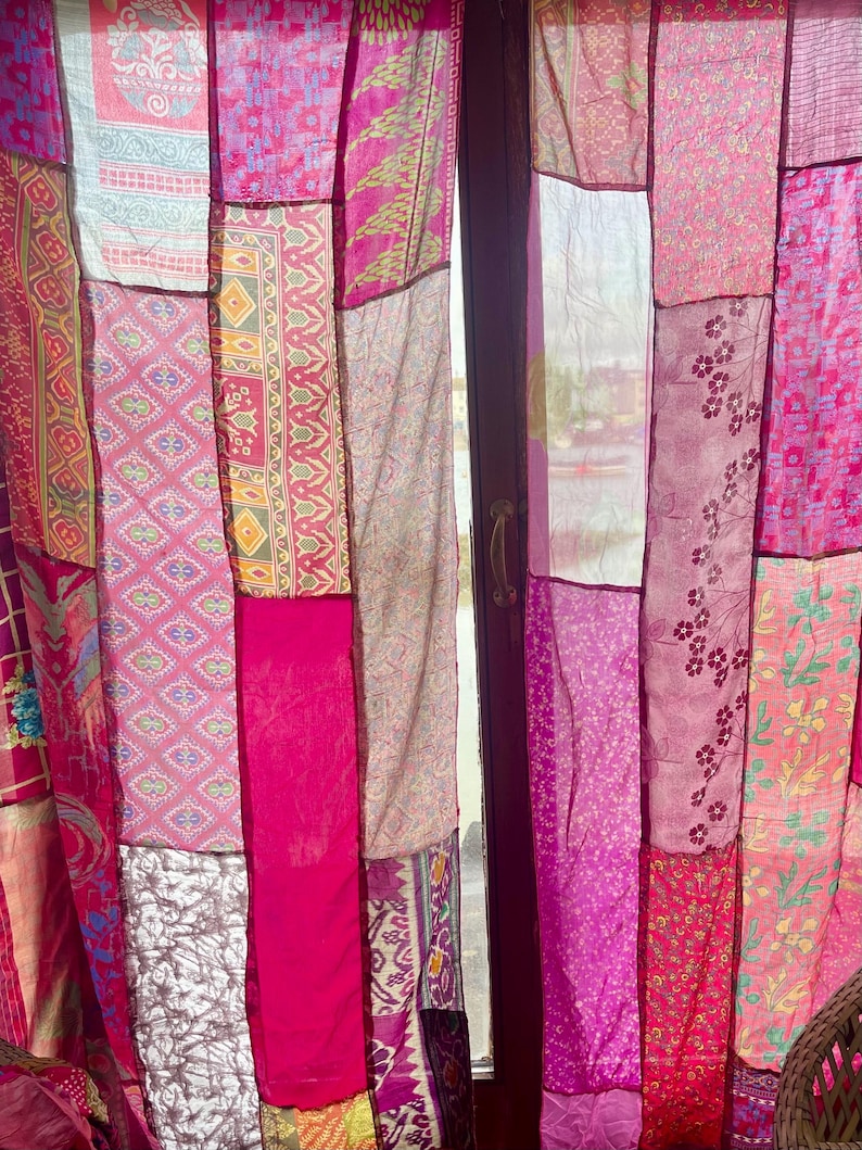 May include: A patchwork curtain made of various pink fabrics. The curtain is composed of rectangular panels with different patterns and shades of pink, creating a vibrant and textured appearance. The curtain hangs in front of a window, allowing light to filter through.