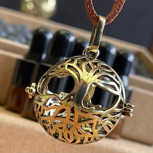 May include: Gold tone tree of life pendant necklace with a round, openwork design. The pendant is attached to a brown leather cord.