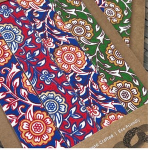 May include: Close-up of several floral patterned bookmarks. The bookmarks feature a repeating design of flowers and leaves in red, blue, gold, and green. The text "Hand Crafted | Eco Friendly" is visible.