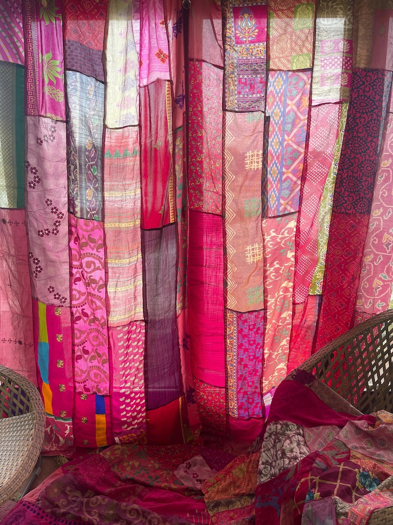 May include: A patchwork curtain made of various fabrics in shades of pink, magenta, and red. The curtain is composed of vertical panels with different patterns and textures, creating a vibrant and eclectic look. The overall theme is bohemian and decorative.