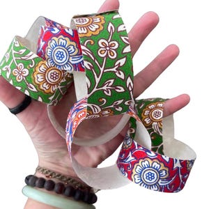 May include: A colorful paper chain with floral patterns in red, green, and yellow. The chain is held in a hand, showcasing the intricate design and vibrant colors. The paper chain is a decorative craft item.