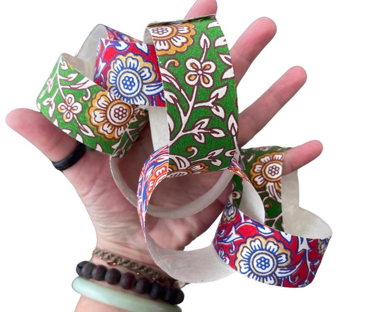 May include: A colorful paper chain with floral patterns in red, green, and yellow. The chain is held in a hand, showcasing the intricate design and vibrant colors. The paper chain is a decorative craft item.