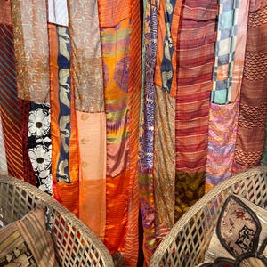Pode incluir: Duas cadeiras de vime com almofadas estampadas est&atilde;o em frente a uma tape&ccedil;aria colorida feita de muitos tecidos diferentes. A tape&ccedil;aria &eacute; feita de uma variedade de cores, incluindo laranja, vermelho, roxo e verde. A tape&ccedil;aria &eacute; feita de uma variedade de tecidos, incluindo seda, algod&atilde;o e veludo.