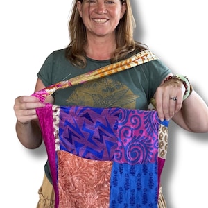 May include: A patchwork shoulder bag featuring a variety of colourful fabric squares in shades of blue, pink, orange, and white. The bag has a wide strap with a repeating leaf pattern and is constructed from multiple distinct textile panels.