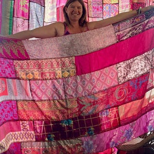 May include: A patchwork textile in shades of pink and magenta, featuring various patterns and textures. The textile is held open, revealing a backdrop of similar fabrics. The overall aesthetic is vibrant and bohemian.