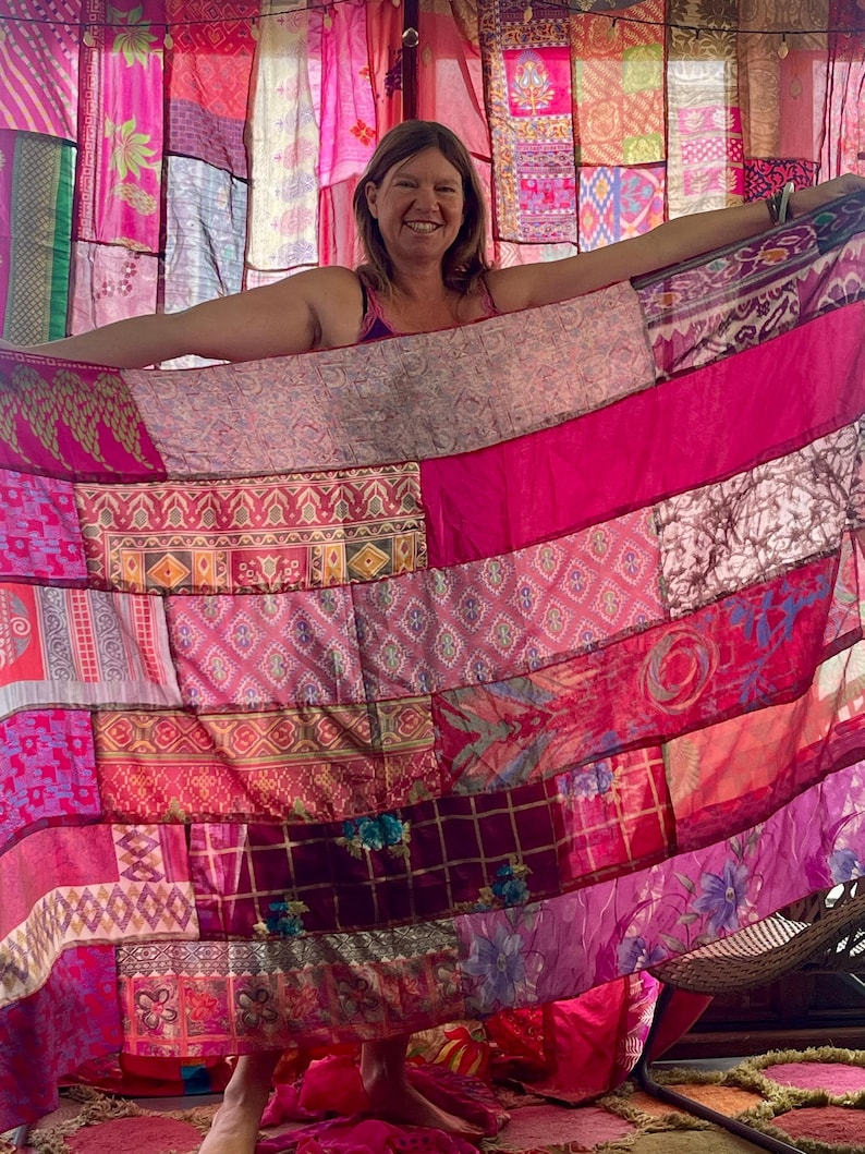 May include: A patchwork textile in shades of pink and magenta, featuring various patterns and textures. The textile is held open, revealing a backdrop of similar fabrics. The overall aesthetic is vibrant and bohemian.