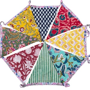 May include: A decorative bunting banner featuring seven triangular fabric flags in various colours including yellow, navy blue, red, green, and teal. Each flag displays a distinct floral or striped pattern, all connected by a pink and white floral trim.