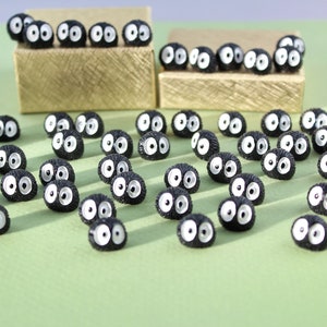 May include: A collection of black and white fuzzy round figurines with large eyes. The figurines are arranged in rows on a green surface.