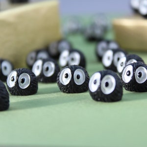 May include: A group of small, black, fuzzy figurines with white eyes. The figurines are arranged on a green surface.