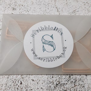 May include: A white envelope with a round sticker that says "ScribbleBox" with a stylized "S" and the website address "www.scribblebox.uk".