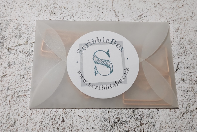 May include: A white envelope with a round sticker that says "ScribbleBox" with a stylized "S" and the website address "www.scribblebox.uk".