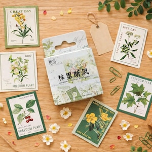 May include: A selection of botanical-themed stationery items on a wooden surface. The set includes decorative cards with floral illustrations, a roll of twine, blank tags, and a box with Chinese text. Green paperclips and a wooden stamp are also present.
