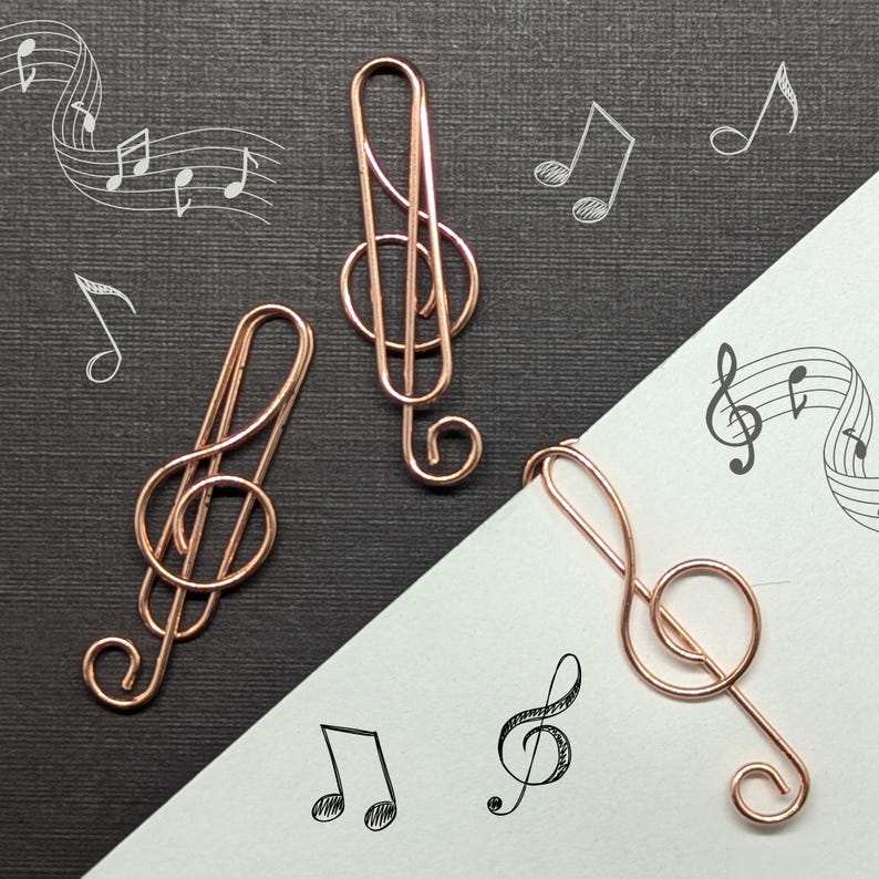 May include: Three rose gold treble clef paper clips on a black and white background. The paper clips are shaped like musical notes.