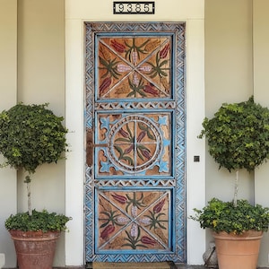 May include: A detailed wooden front door, painted in blue and brown, with carved floral and geometric patterns. The door has the number "9385" above it. Two potted trees sit either side of the door on a brick porch.