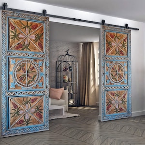 May include: Two wooden barn doors with a distressed, hand-painted design. The doors feature a repeating pattern of flowers and geometric shapes in shades of blue, orange, and green. The doors are mounted on a black sliding track.